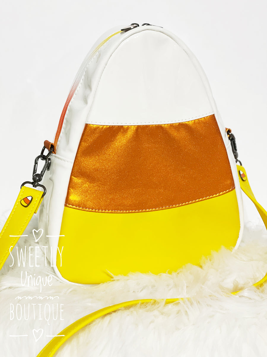 candy corn shaped purse on white background with yellow strap, yellow bottom, orange middle, white top and body. gunmetal hardware, candy corn chicago screws on straps sitting on white fur